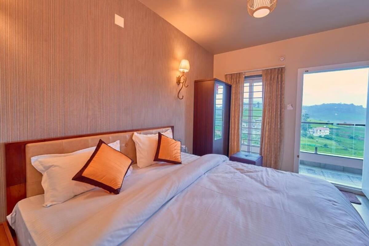 A hotel room with a large bed, a nightstand, a wall-mounted lamp, and a window with curtains.