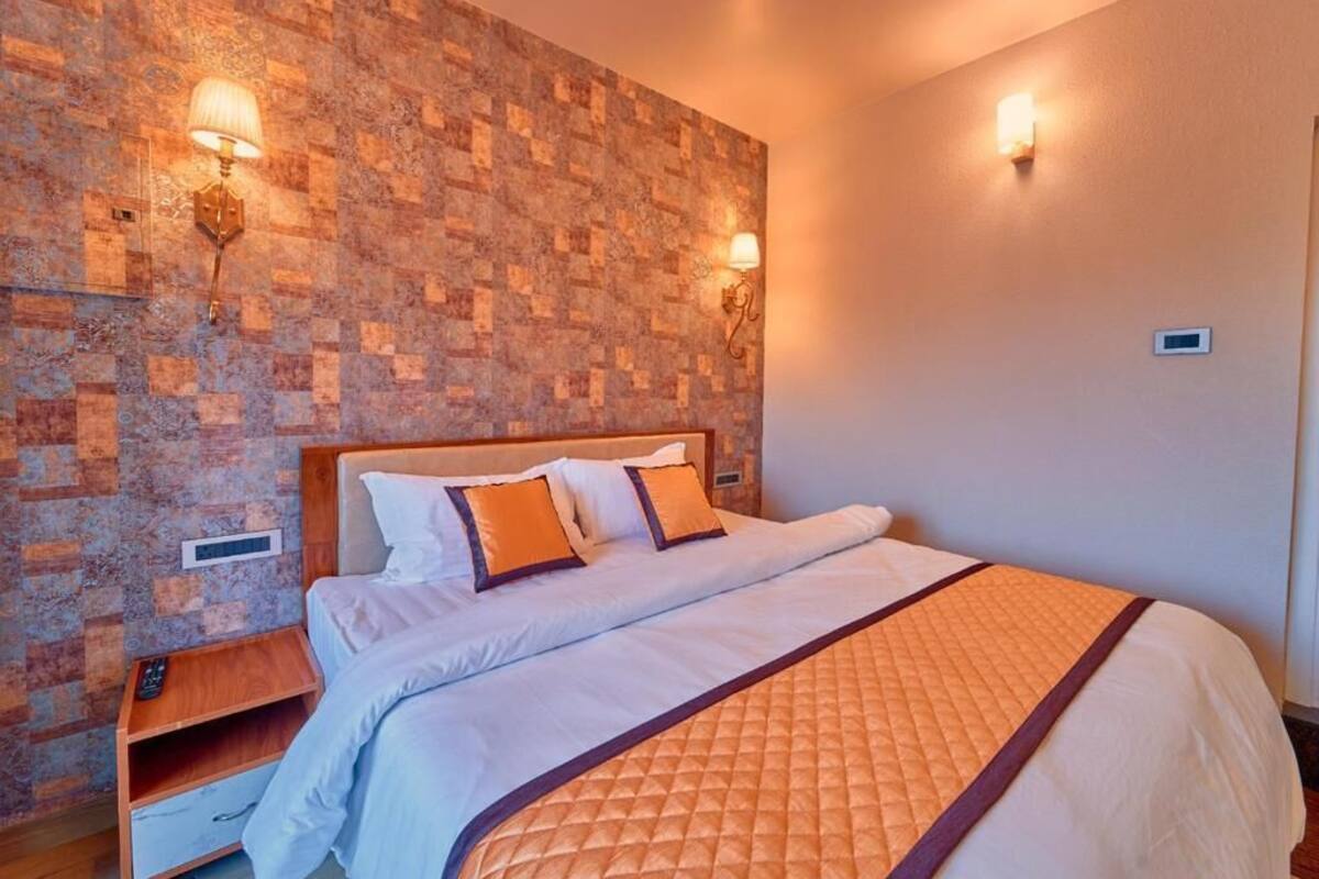 Ein Hotelzimmer mit einer Wand im Ziegelstein-Muster, einem Bett mit weißer Bettwäsche und orangefarbenen Akzenten, zwei Wandleuchten und einem Holfnachtkästchen.