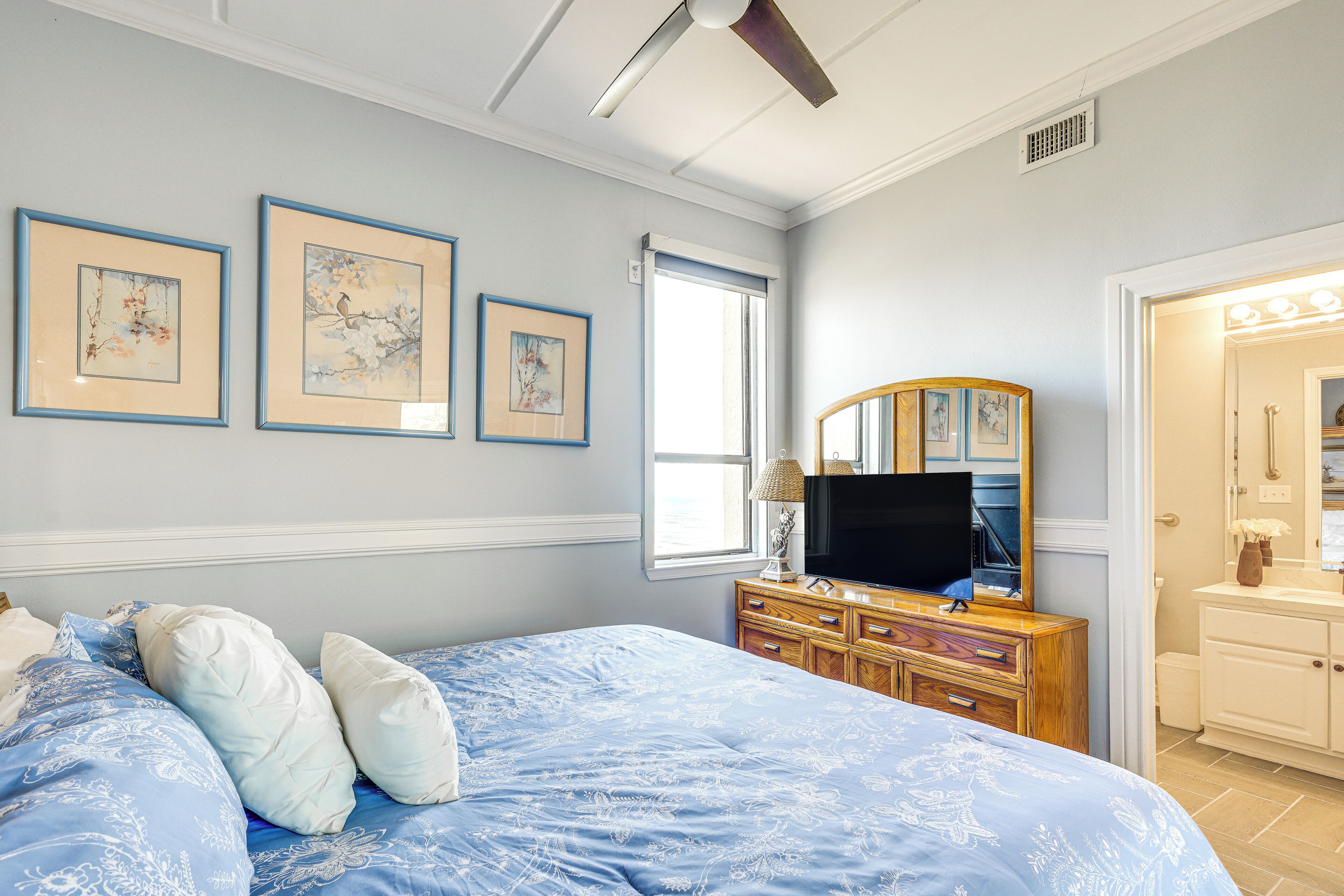 Un dormitorio con cama, cómoda, televisor y cuadros en la pared.
