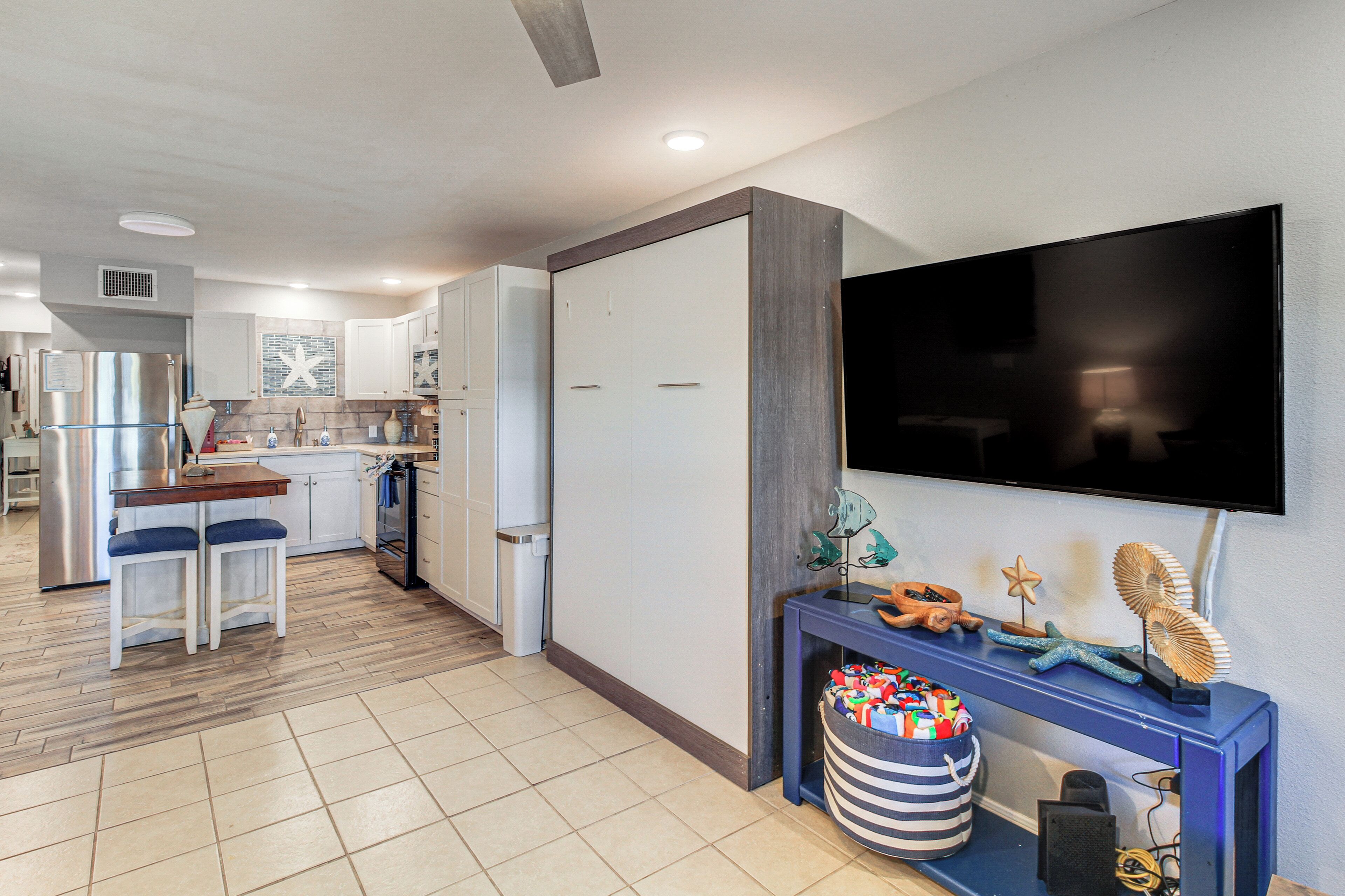 A modern kitchen with white cabinets, a stainless steel refrigerator, and a dining area with two blue chairs.