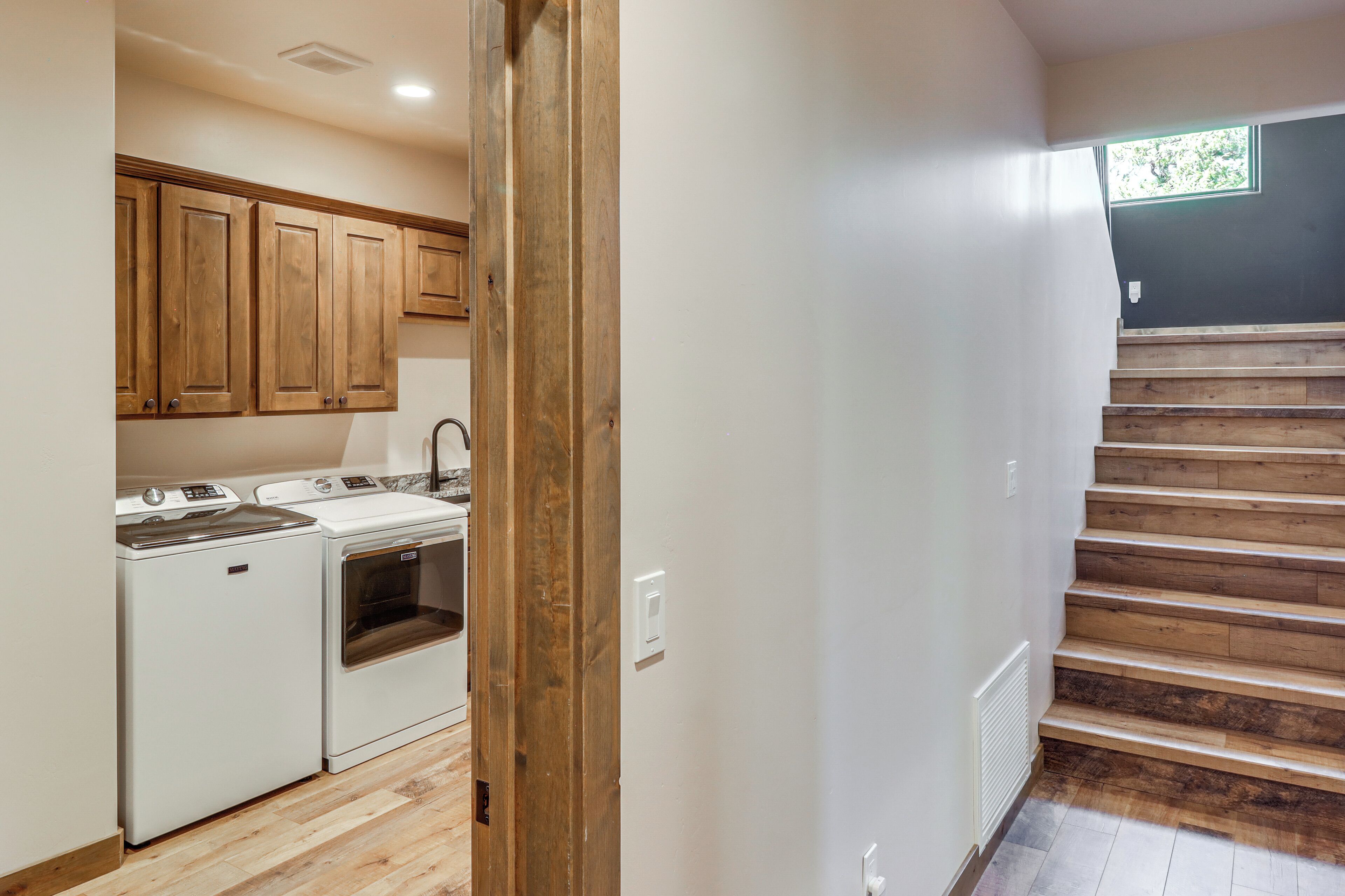 A laundry area with a washer and dryer, wooden cabinets, and a staircase leading to an upper level.