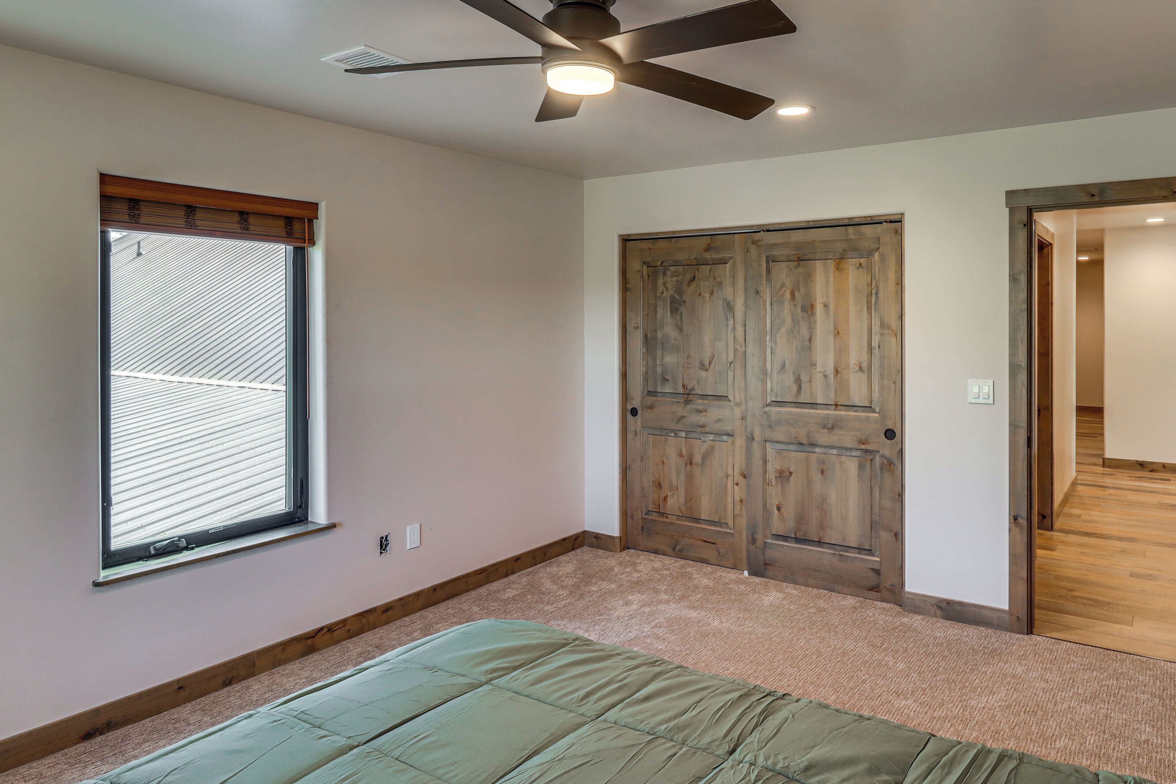 A bedroom with a bed, a ceiling fan, a window with blinds, and a wooden door.