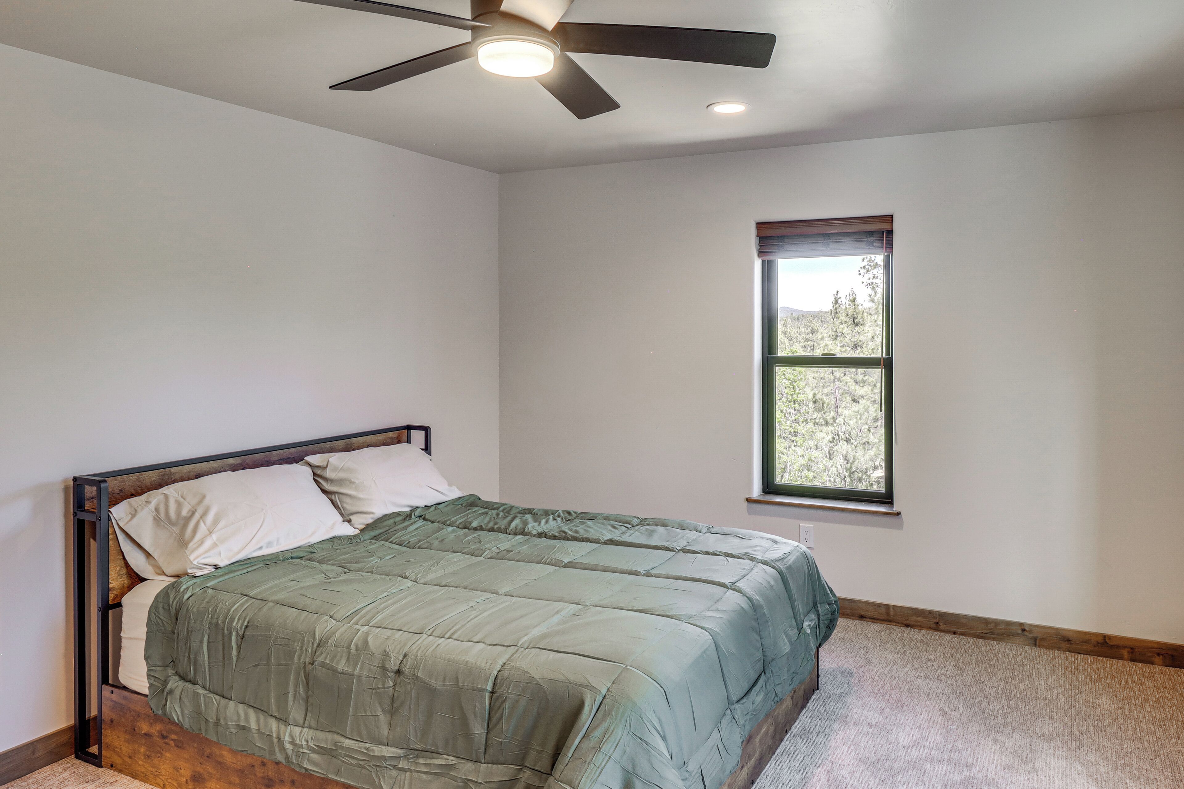 A bedroom with a bed, a ceiling fan, a window, and a carpeted floor.