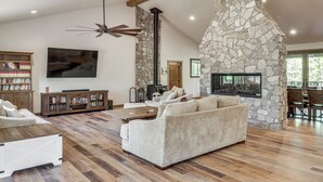 A spacious living room with a stone fireplace, a large sofa, a wooden coffee table, and a ceiling fan. - Spacious Family Gem w/ Patio, 3 Mi to Rainbow Lake (Lakeside)