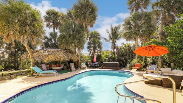 A swimming pool with lounge chairs and umbrellas, surrounded by palm trees. - Steps to Sand! Pet-friendly Home in Fort Pierce (Fort Pierce)