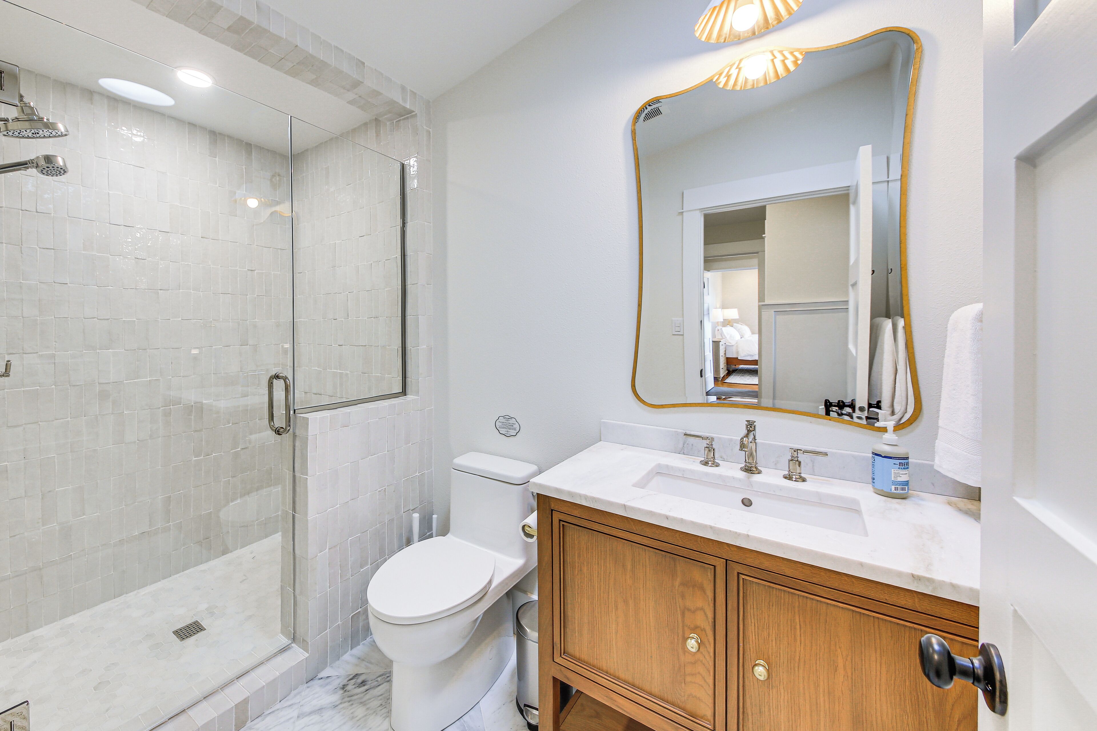 A bathroom with a glass-enclosed shower, a toilet, a sink with a mirror, and wooden cabinets.