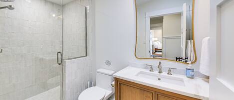 A bathroom with a glass-enclosed shower, a toilet, a sink with a mirror, and wooden cabinets.