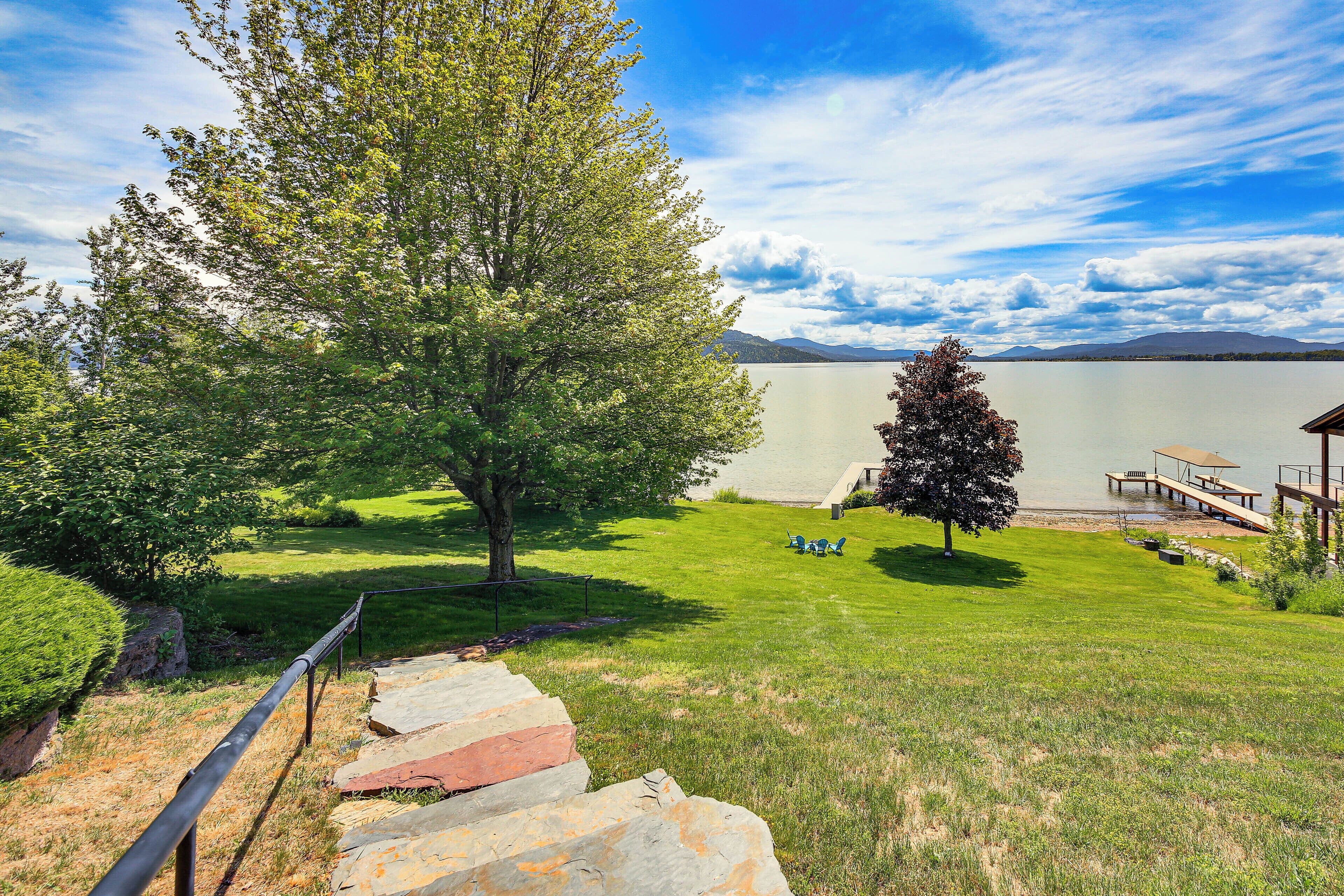 A grassy area with a wooden deck, a stone staircase, and a view of a lake and mountains.
