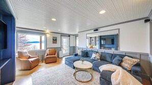 A modern living room with a sectional sofa, a round coffee table, and a large window offering a view. - Stunning Sandpoint Lakefront Home: Hot Tub + Dock (Sandpoint)