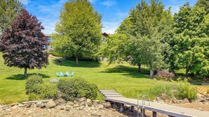 A serene park with a wooden deck, stone pathway, and a small bridge over water. - Stunning Sandpoint Lakefront Home: Hot Tub + Dock (Sandpoint)