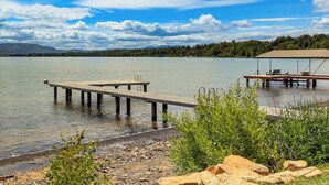A lakeside dock with a covered seating area, a wooden pier, and a rocky shoreline. - Stunning Sandpoint Lakefront Home: Hot Tub + Dock (Sandpoint)