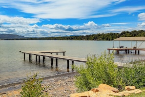 A lakeside dock with a covered seating area, a wooden pier, and a rocky shoreline.
