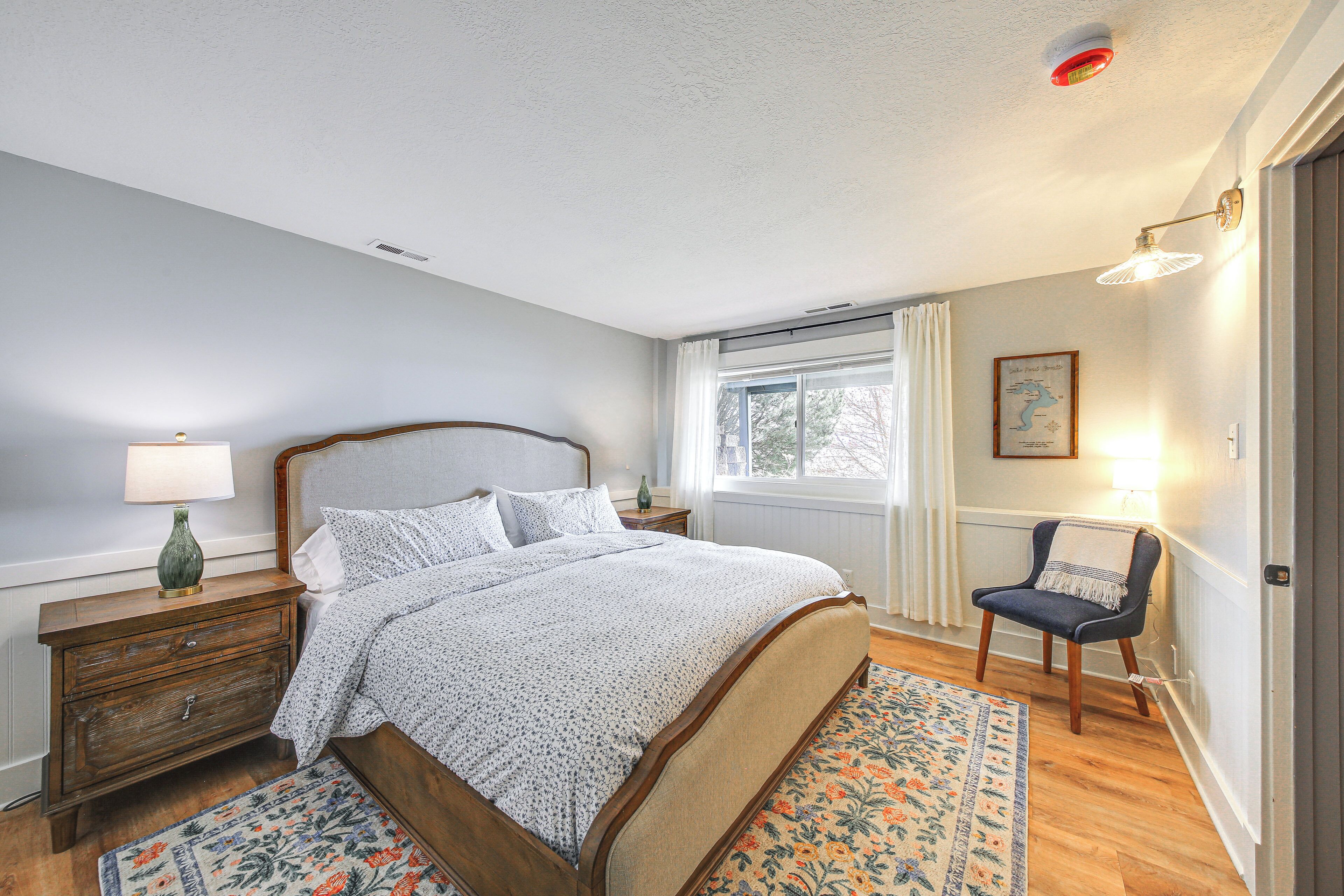 A bedroom with a bed, nightstand, chair, window, and a rug.