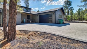 A modern two-story house with a garage, a paved driveway, and a landscaped yard with pine trees. - Modern Luxury in Torreon w/ HOT Tub! (Show Low)
