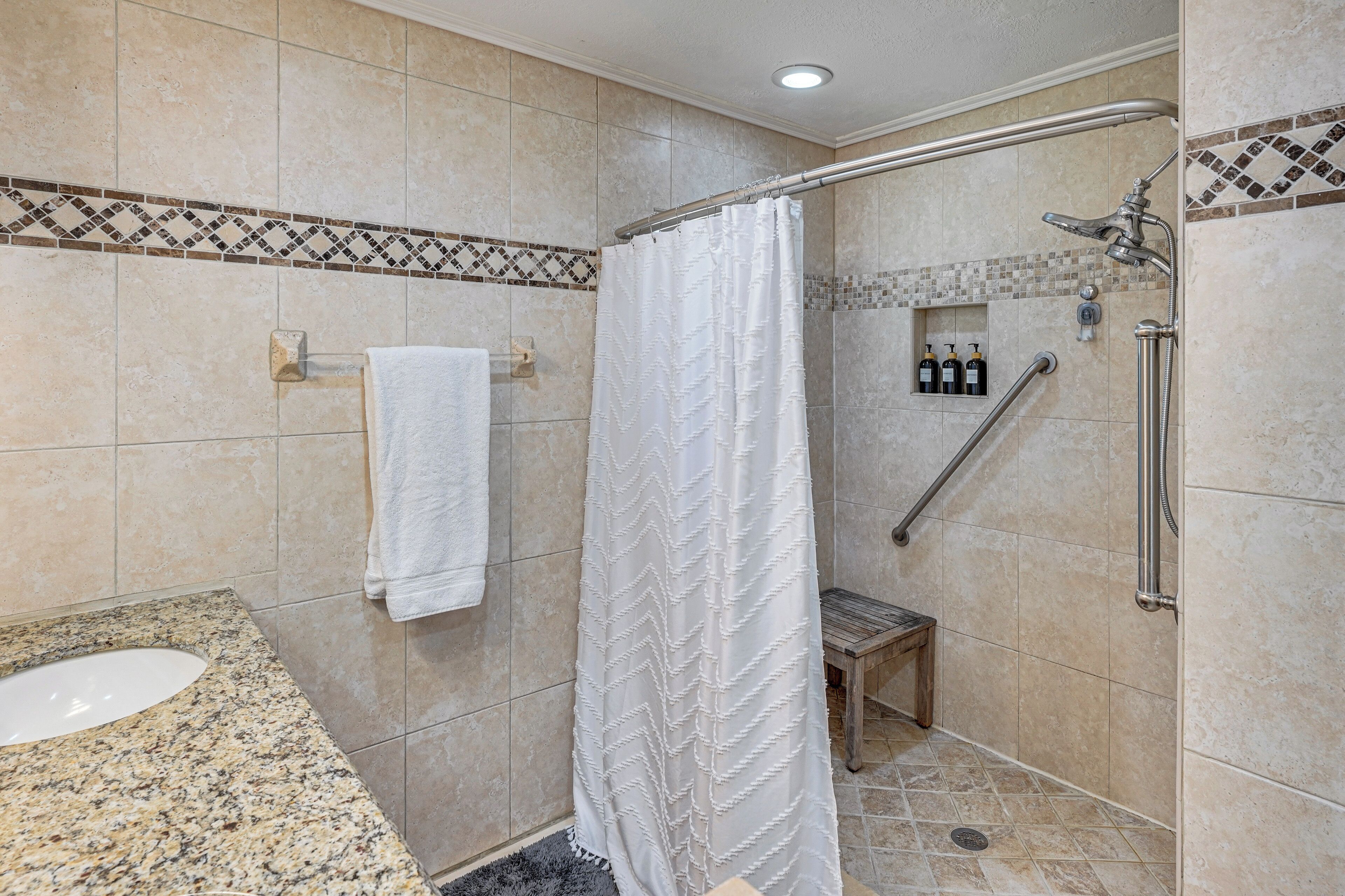 A bathroom with a shower, a sink, and a bench.