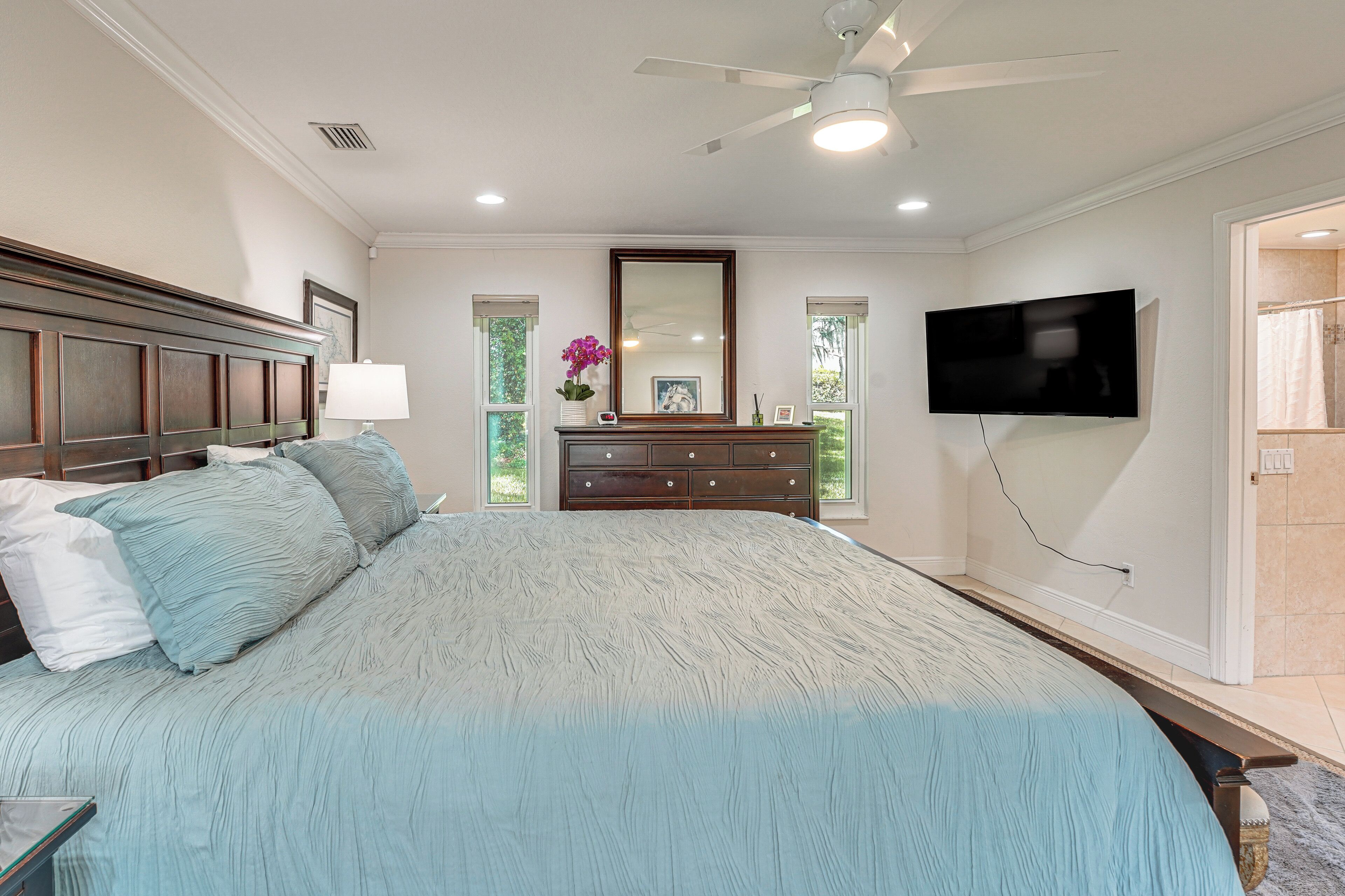 Une chambre à coucher avec un grand lit, une commode, un téléviseur et un ventilateur de plafond.