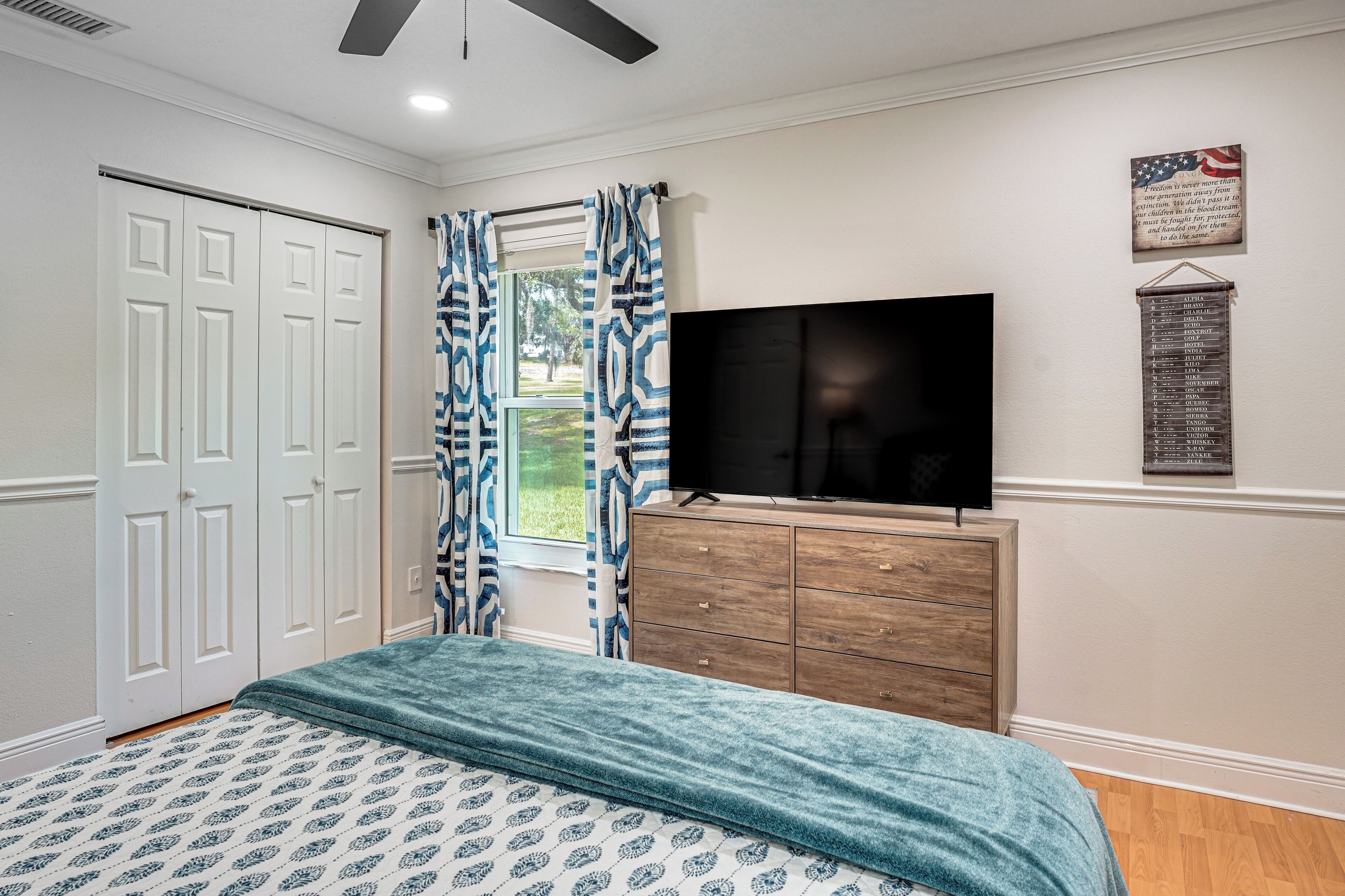 A bedroom with a bed, a dresser, a TV, and a window with curtains.