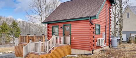 A log cabin with a wooden deck, a front door, and a chimney.