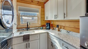 A kitchen with wooden walls, white cabinets, a stainless steel refrigerator, and a window with a view of trees. - Handcrafted Tiny Home, Near Dtwn Boone (Boone)