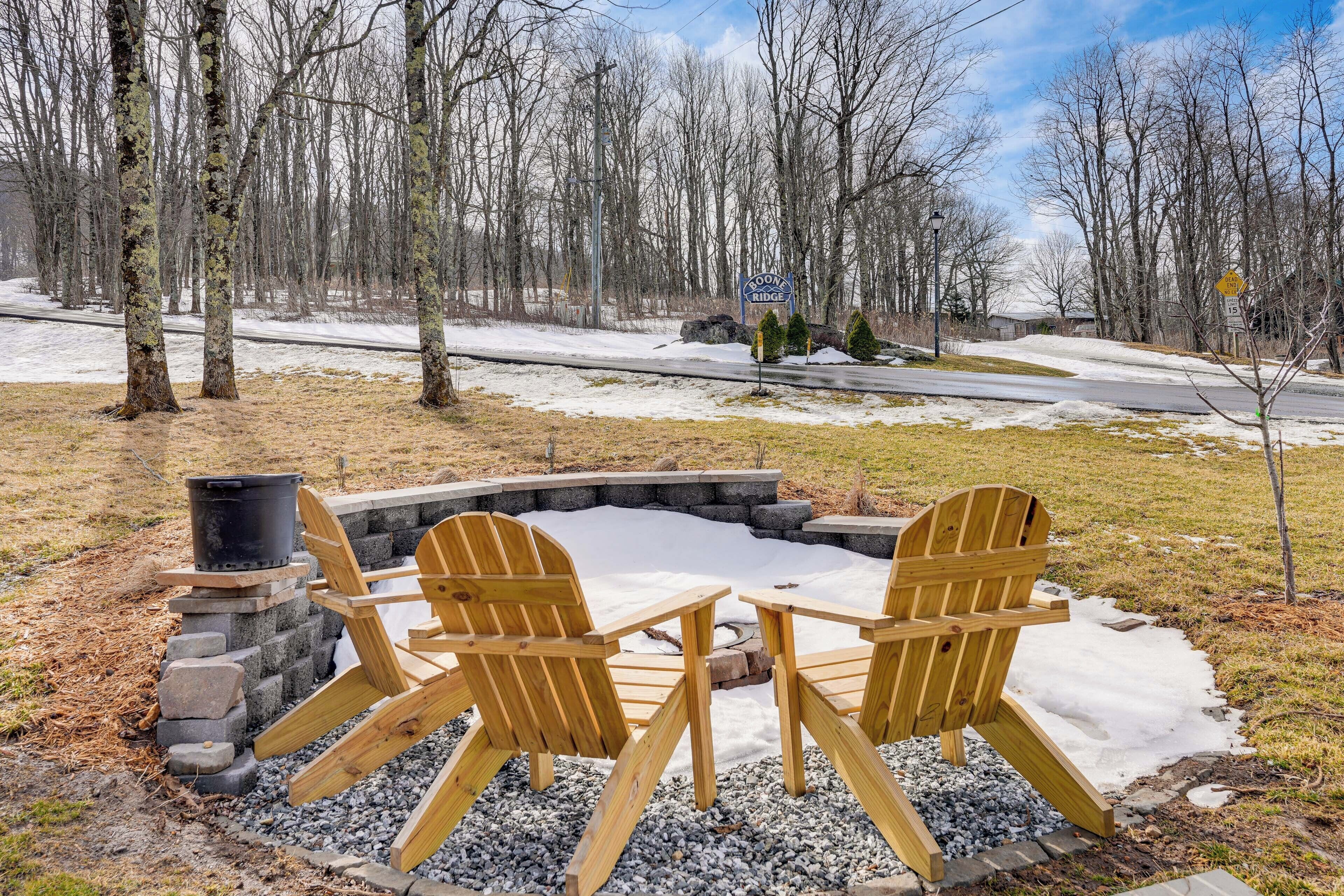 A snow-covered outdoor seating area with Adirondack chairs and a fire pit.