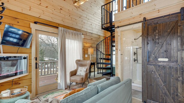 A wooden cabin interior with a sofa, armchair, TV, and a staircase leading to a balcony. - Handcrafted Tiny Home, Near Dtwn Boone (Boone)