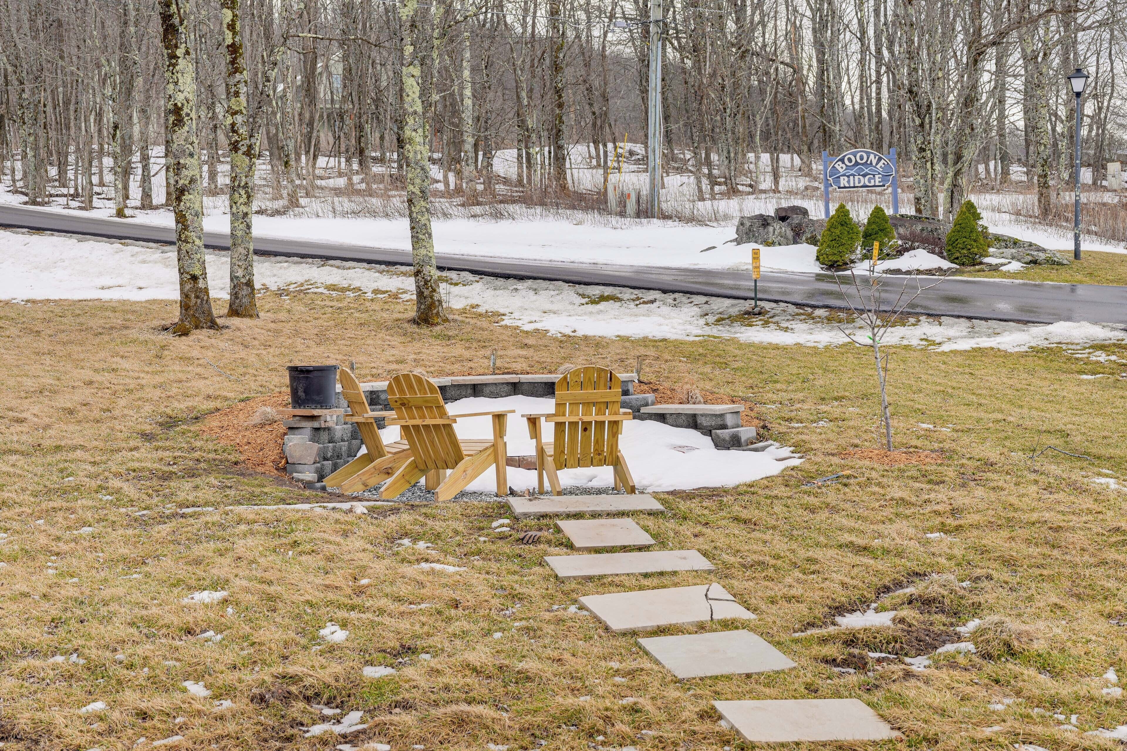 Ulkoalue, jossa on puinen istuinalue, Adirondack-tyyliset tuolit ja kivinen nuotiopaikka. Alue on lumipeitteisen maan ja puiden ympäröimä.