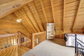 Un dormitorio de buhardilla con suelo de madera, techo inclinado, una cama, un estante blanco y una escalera.