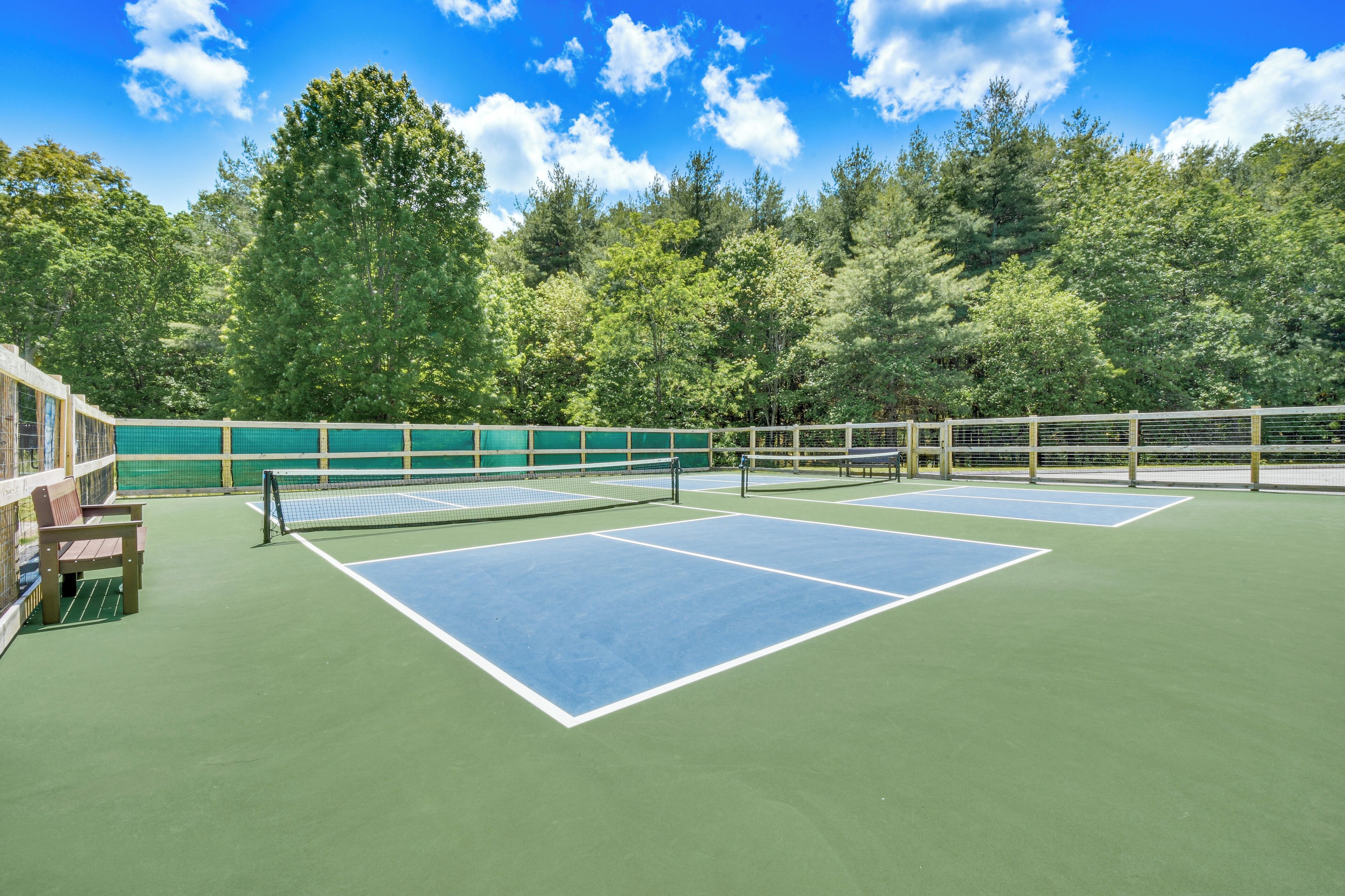 Una cancha de tenis al aire libre con red, rodeada por una valla de madera y bancos.