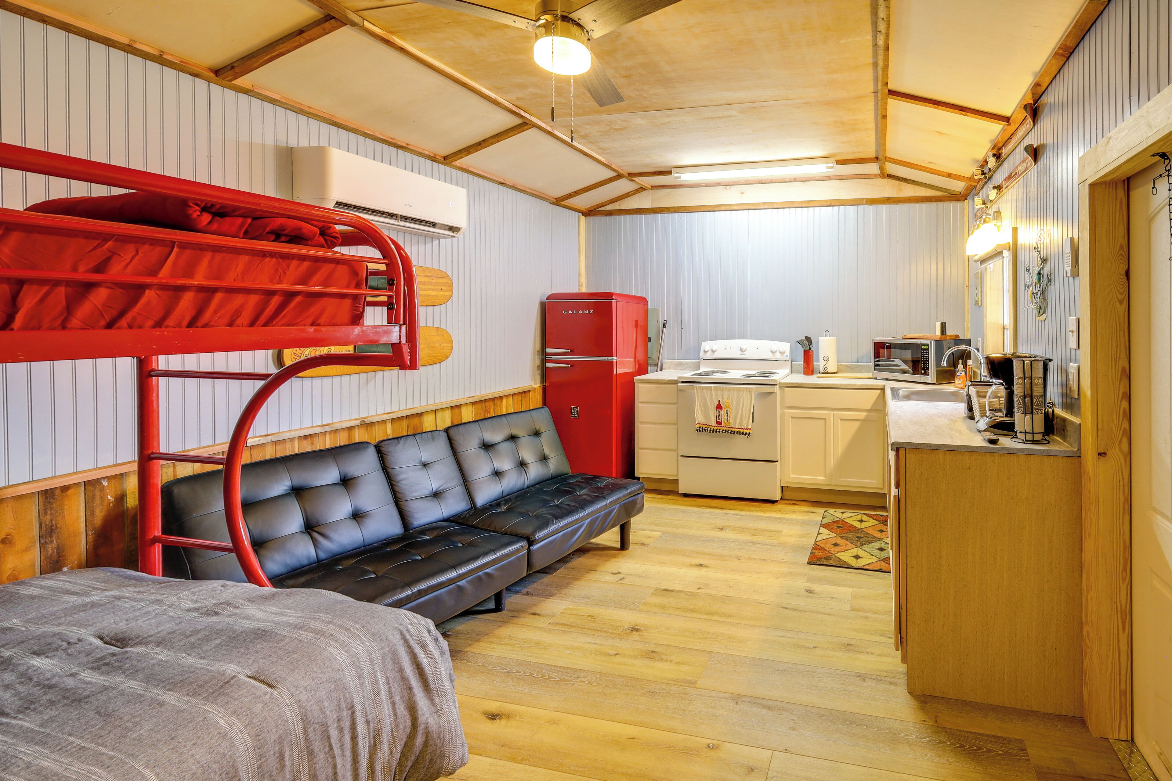 A compact room with bunk beds, a sofa, a kitchenette, and a wooden ceiling.