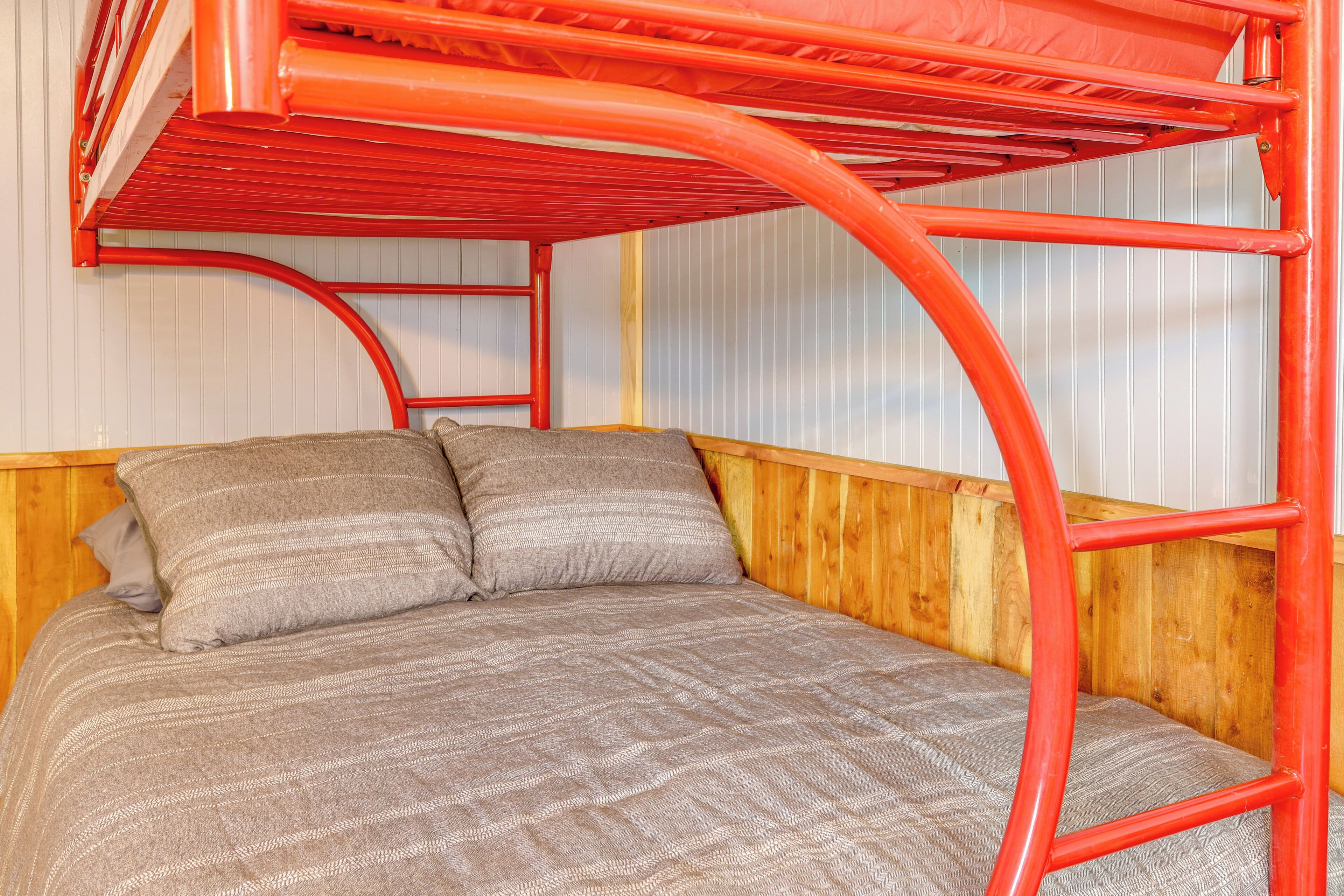 Un lit superposé avec une structure rouge, une tête de lit en bois et une couverture à motifs gris.