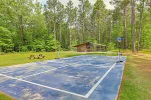 Una cancha de tenis con una mesa de picnic, rodeada por un bosque.
