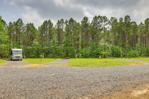 A gravel parking area with a bus and a forested backdrop.