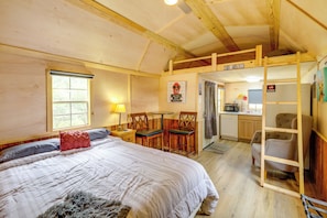 A bedroom with a bed, a desk, and a chair. There is a window and a door.