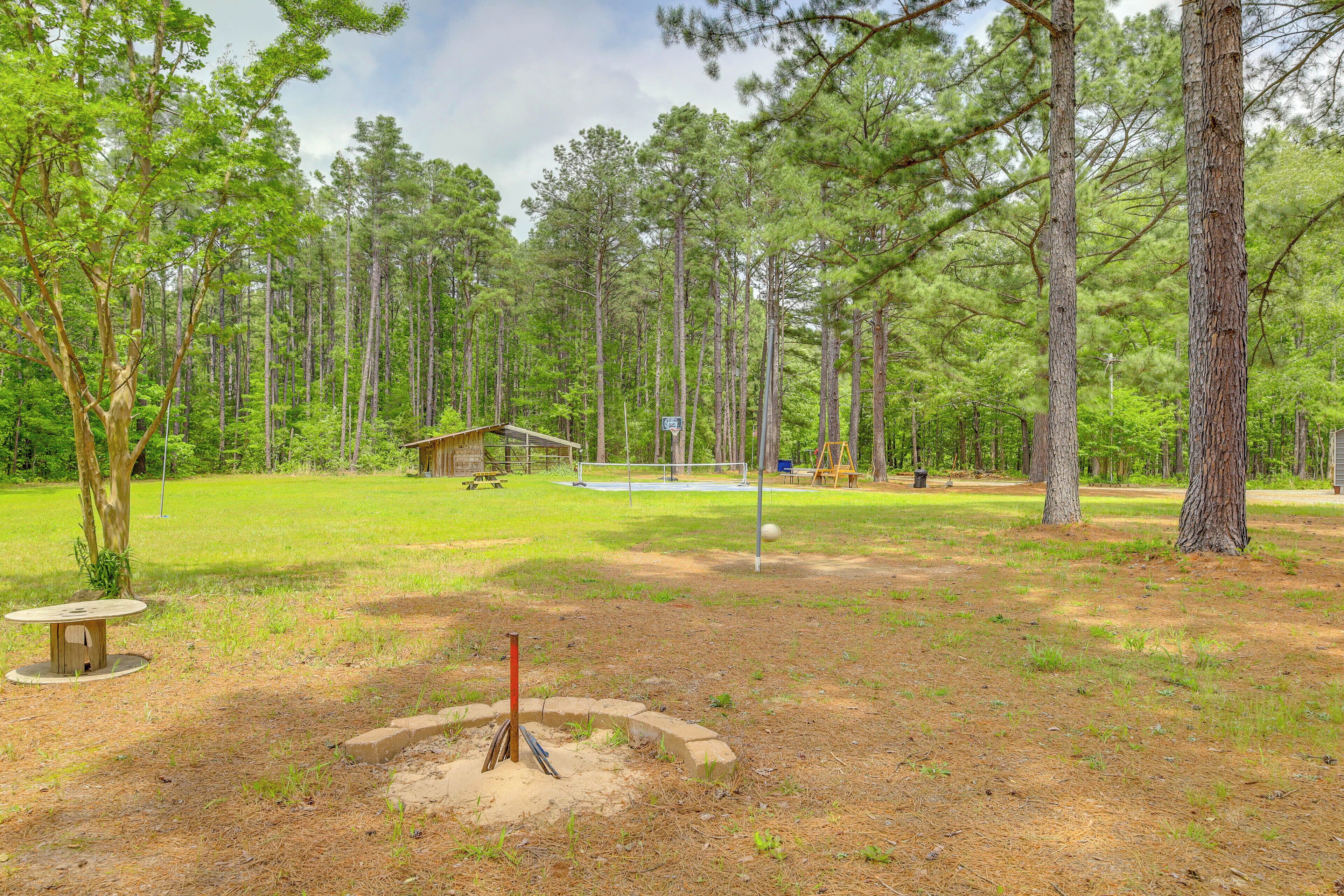 A forested area with a small cabin, a volleyball net, and a disc golf tee.