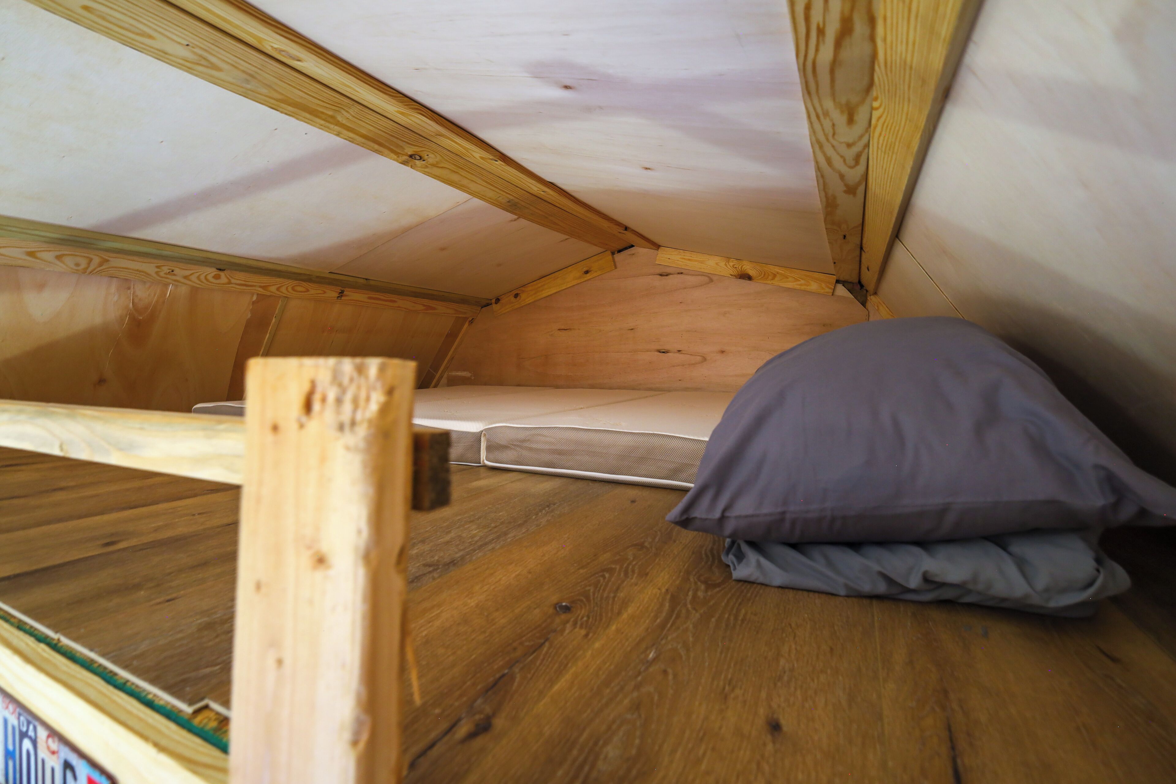 A small, wooden attic room with a mattress and a pillow.
