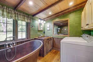 Un baño rústico con una bañera grande, armarios de madera y una ventana con vistas.
