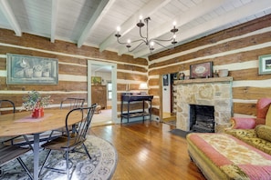 A log cabin interior with a dining table, chairs, a sofa, a fireplace, and a chandelier. - Trout Stream Access! Rural Buchanan Cabin (Buchanan)