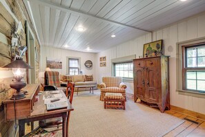 A cozy living room with a fireplace, a sofa, a plaid armchair, and a wooden cabinet. - Trout Stream Access! Rural Buchanan Cabin (Buchanan)
