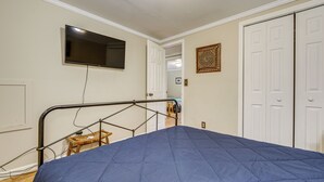 Een slaapkamer met een bed, een aan de muur bevestigde televisie, een deur en een klein krukje.
