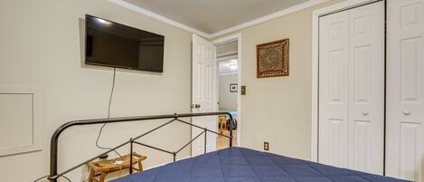 A bedroom with a bed, a television mounted on the wall, a door, and a small stool.