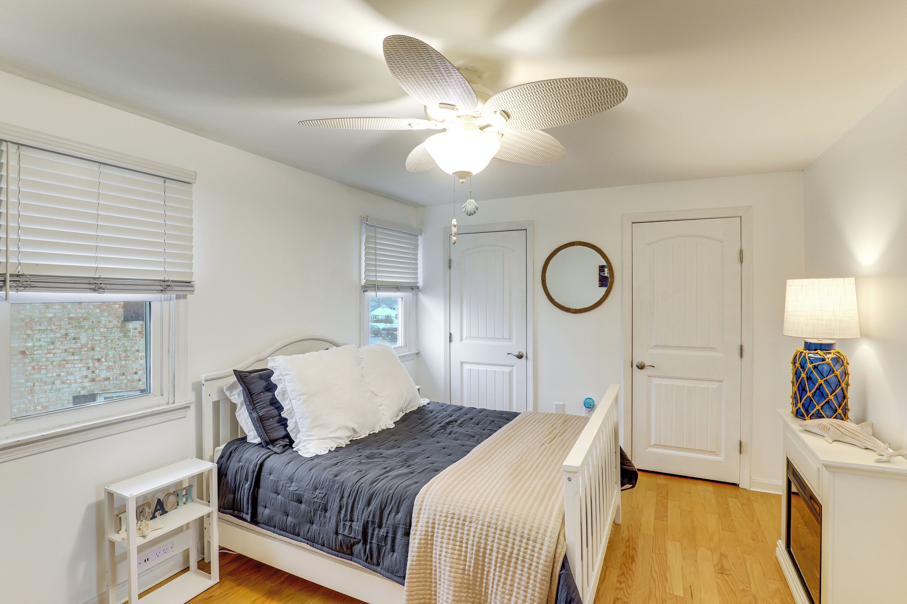 A bedroom with a bed, a ceiling fan, a window, a door, and a lamp.
