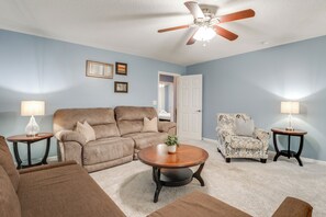 A living room with a brown sofa, a patterned armchair, a coffee table, and two side tables with lamps. - Modern 6BR Haven With Playroom, Gym, Deck (Cartersville)