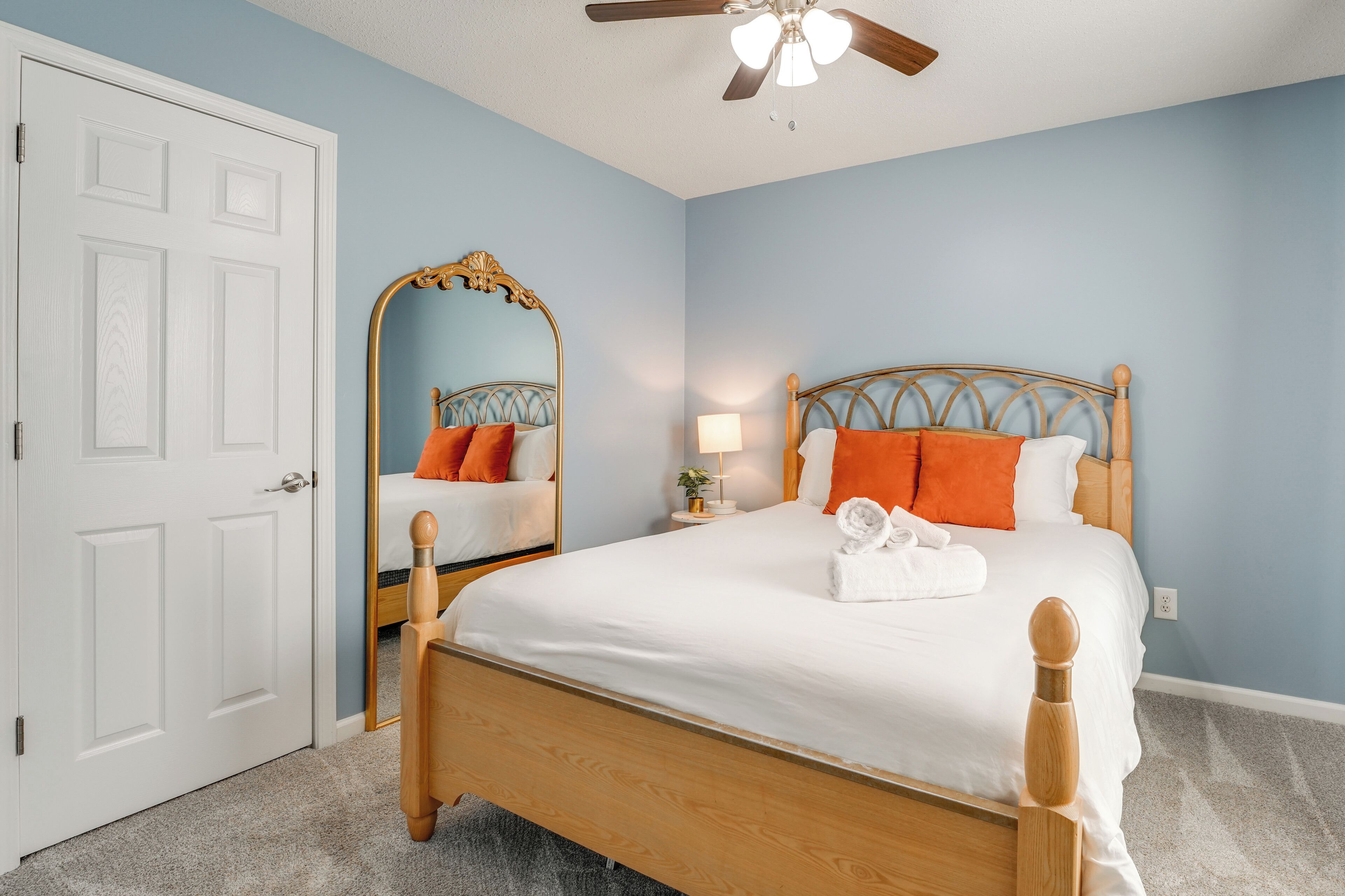 A bedroom with a wooden bed, a white door, a ceiling fan, and a mirror.