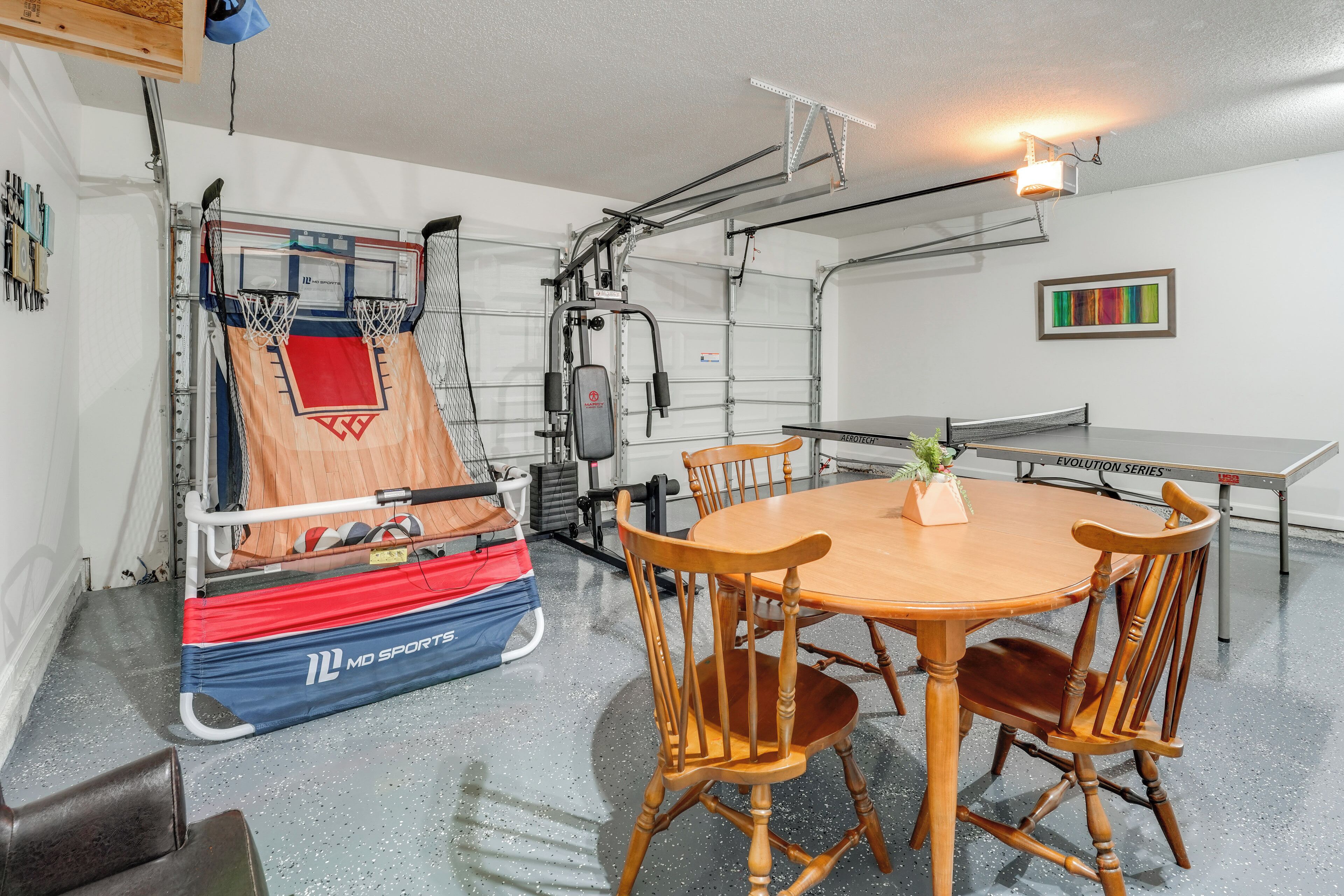 A gym with exercise equipment, a basketball hoop, and a dining area with a table and chairs.
