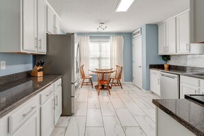 A modern kitchen with white cabinets, a granite countertop, a stainless steel refrigerator, and a dining table with chairs. - Modern 6BR Haven With Playroom, Gym, Deck (Cartersville)
