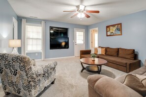 A living room with a ceiling fan, a flat-screen TV, a brown sofa, a patterned armchair, and a coffee table. - Modern 6BR Haven With Playroom, Gym, Deck (Cartersville)