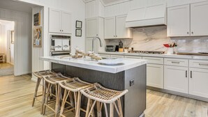 A kitchen with white cabinets, a marble countertop, a stainless steel range, and a central island with bar stools. - A-frame Waterfront Escape on Lochada Lake (Glen Spey)