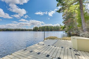 Un muelle de madera que se adentra en un lago, con cielo despejado y árboles al fondo.