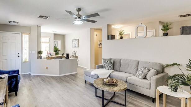 Ein modernes Wohnzimmer mit einem grauen Sofa, einem runden Couchtisch und einem Deckenventilator.