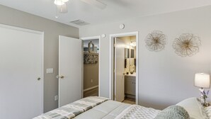 Ein Schlafzimmer mit einem Bett, einem Nachttisch mit Lampe, einer Tür zu einem Badezimmer und einer Wand mit zwei Dekorationselementen.